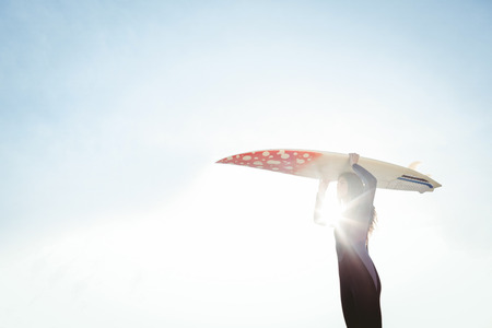 Woman in wetsuit with a surfboard on a sunny day at the beachの写真素材