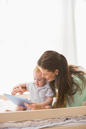 Happy mother using tablet with his baby boy at home in bedroomの写真素材