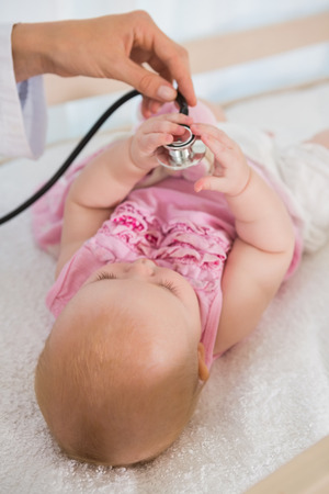 Beautiful cute baby girl with doctor with stethoscope at home in bedroomの写真素材