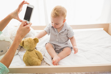 Happy mother taking a picture of her baby boy at home in bedroomの写真素材