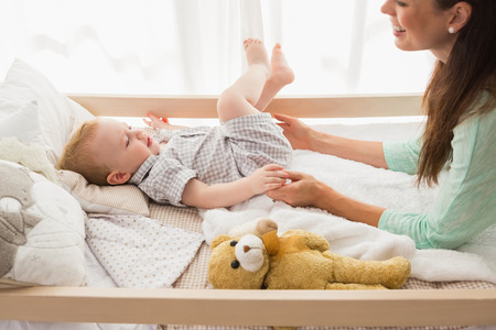 Happy mother with her baby boy at home in bedroomの写真素材
