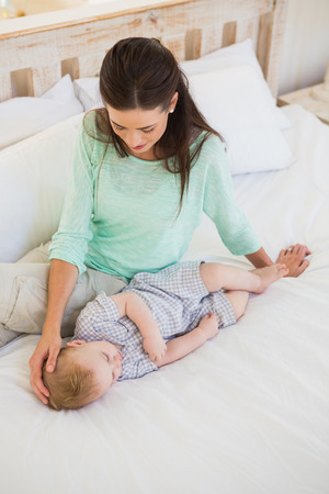 Happy mother with her baby boy at home in bedroomの写真素材