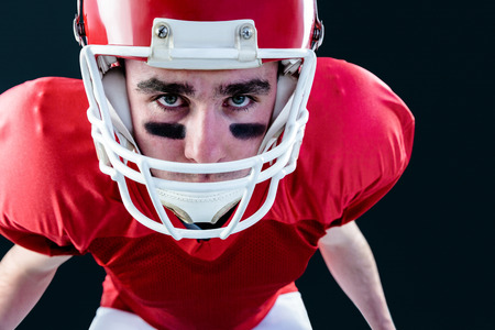 Portrait of a serious american football player taking his helmet looking at camera with black backgroundの写真素材