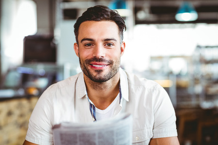 Young man having cup of coffee reading newspaper at the cafeの写真素材