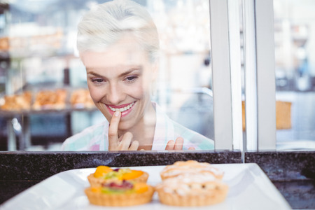 Hesitating pretty woman looking at fruit pie at the bakeryの写真素材