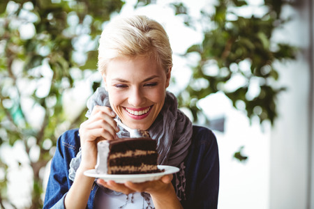 Smiling blonde taking a piece of chocolate cake at the cafeの写真素材