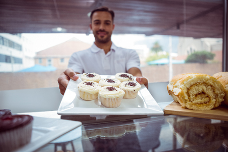 Smiling worker holding cupcakes behind the counter at bakeryの写真素材
