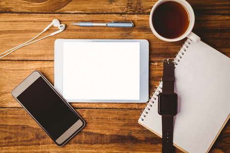`Tablet ans smartphone and swatch on notepad next to cup of coffee on wooden table