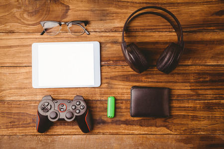 Tablet and music headphone next the joystick USB key and glasses on wooden table
