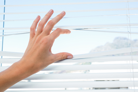 Curious person watching through venetian blind on a sunny dayの写真素材