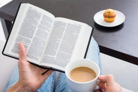 Woman reading a book and holding cup of coffee on the couchの写真素材