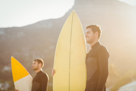 Two men in wetsuits with a surfboard on a sunny day at the beachの写真素材