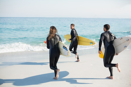 Group of friends on wetsuits with a surfboard on a sunny day at the beachの写真素材