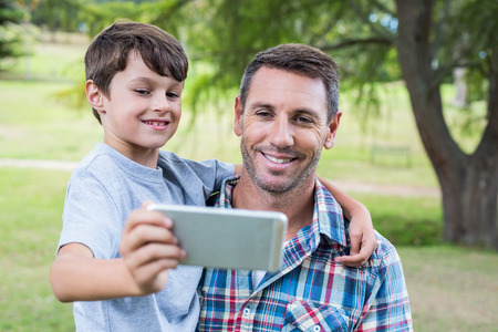 Father and son taking a selfie in the park on a sunny dayの写真素材