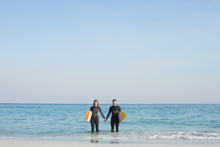happy couple in wetsuits with surfboard on a sunny day at the beachの写真素材