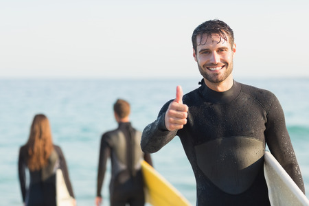 Group of friends on wetsuits with a surfboard on a sunny day at the beachの写真素材
