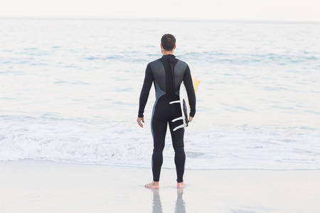 Man in wetsuit with a surfboard on a sunny day at the beachの写真素材