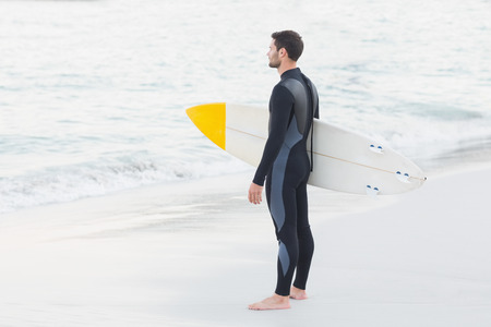 Man in wetsuit with a surfboard on a sunny day at the beachの写真素材