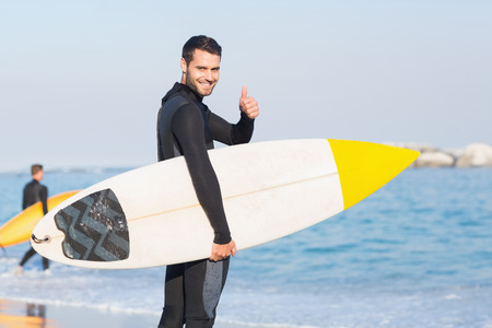 Man in wetsuit with a surfboard on a sunny day at the beachの写真素材
