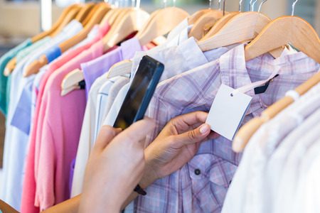 Woman scanning bar code with her mobile phone in clothes store