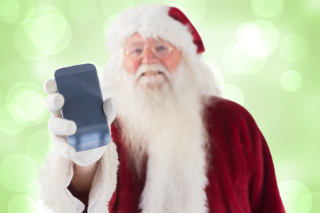 Santa Claus shows a smartphone against green abstract light spot designの写真素材