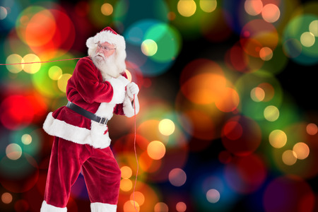 Santa pulls something with a rope against colourful glowing dots on blackの写真素材