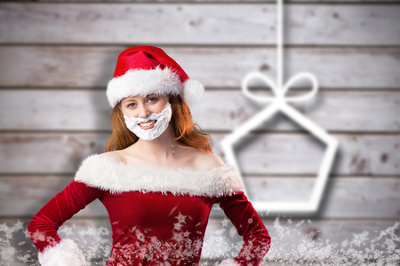 Festive redhead in foam beard against blurred christmas decorations on woodの写真素材