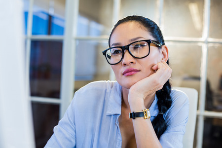 Thoughtful businesswoman sitting at her desk in the officeの写真素材