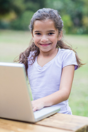 Little girl using her laptop in a park on a sunny dayの写真素材
