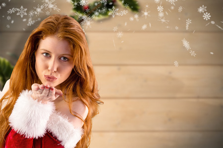 Festive redhead blowing a kiss against blurred holly on woodの写真素材