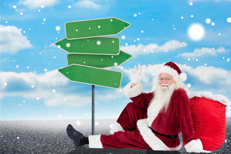Santa sits leaned on his bag and waves against illustration of empty signpostsの写真素材