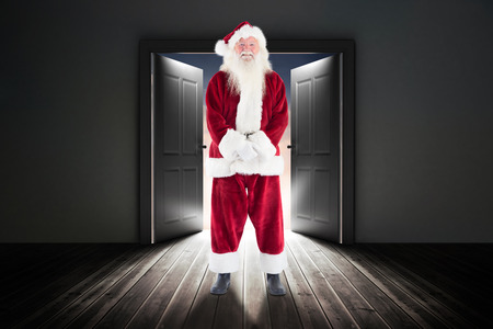 Jolly Santa smiling at camera against open doors in dark roomの写真素材
