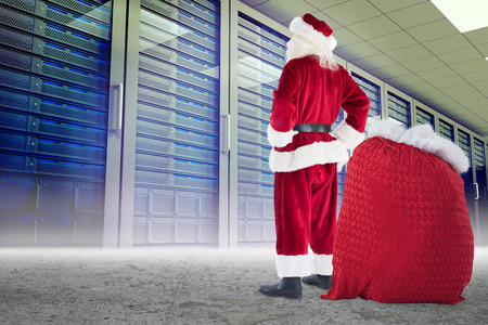 Happy santa with sack of gifts against server towers in desert setting