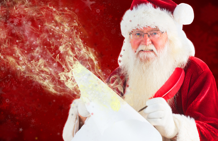 Santa claus writing on scroll against blurred snowflake designの写真素材
