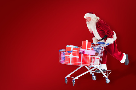 Santa pushes a shopping cart against red backgroundの写真素材