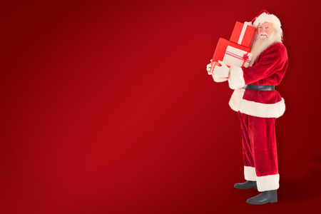 Santa carries a few presents against red backgroundの写真素材