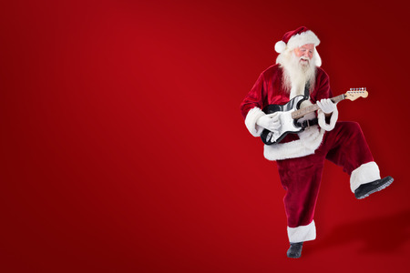 Santa Claus has fun with a guitar against red backgroundの写真素材