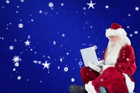 Santa sits and uses a laptop against blue snowflake backgroundの写真素材