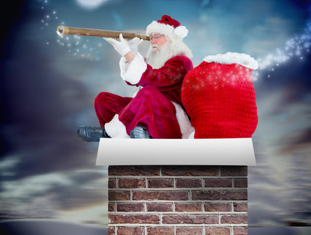 Santa claus looking through telescope against snowy landscape with fir treesの写真素材