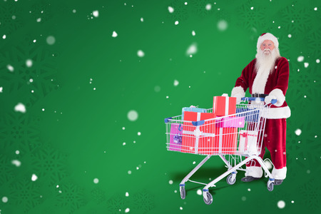 Santa pushes a shopping cart with presents against green snowflake backgroundの写真素材