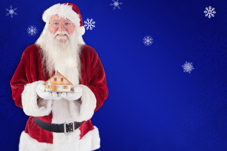 Santa holds a tiny house in his hands against blue snowflake backgroundの写真素材