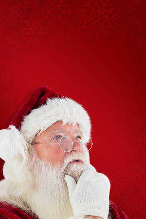 Santa is thinking about something against red backgroundの写真素材
