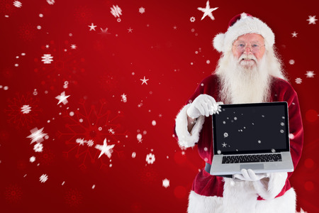 Santa Claus presents a laptop against red snowflake backgroundの写真素材