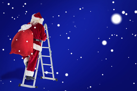 Santa steps up a ladder against blueの写真素材