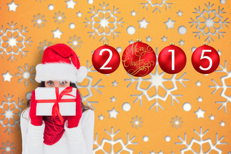 Brunette in red gloves and santa hat showing gift against snowflake wallpaper patternの写真素材