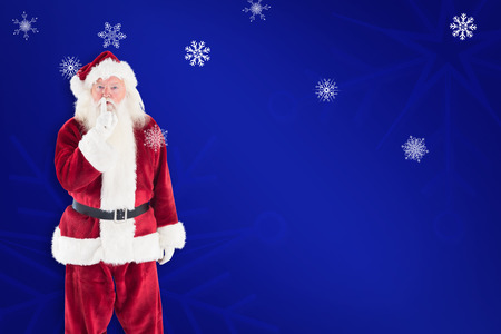 Santa asking for quiet to camera against blue snowflake backgroundの写真素材
