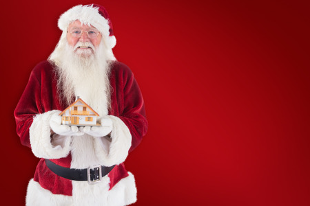 Santa holds a tiny house in his hands against red backgroundの写真素材