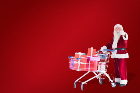 Santa likes to push a shopping cart with presents against red backgroundの写真素材
