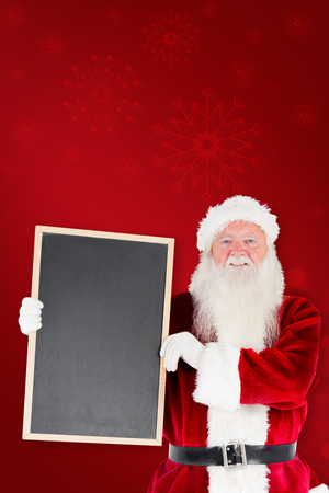Santa claus showing blackboard against red backgroundの写真素材