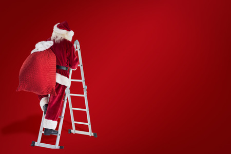 Santa steps up a ladder against red backgroundの写真素材
